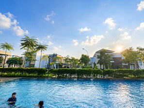 Une piscine où se trouvent deux personnes, entourée de verdure et de bâtiments.