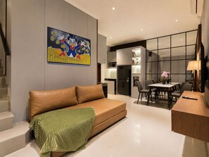 Una sala moderna con un sofá, un comedor con mesa y sillas, una zona de cocina y una obra de arte grande en la pared.