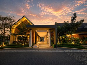 Un edificio moderno con una galería techada y columnas, rodeado de vegetación.