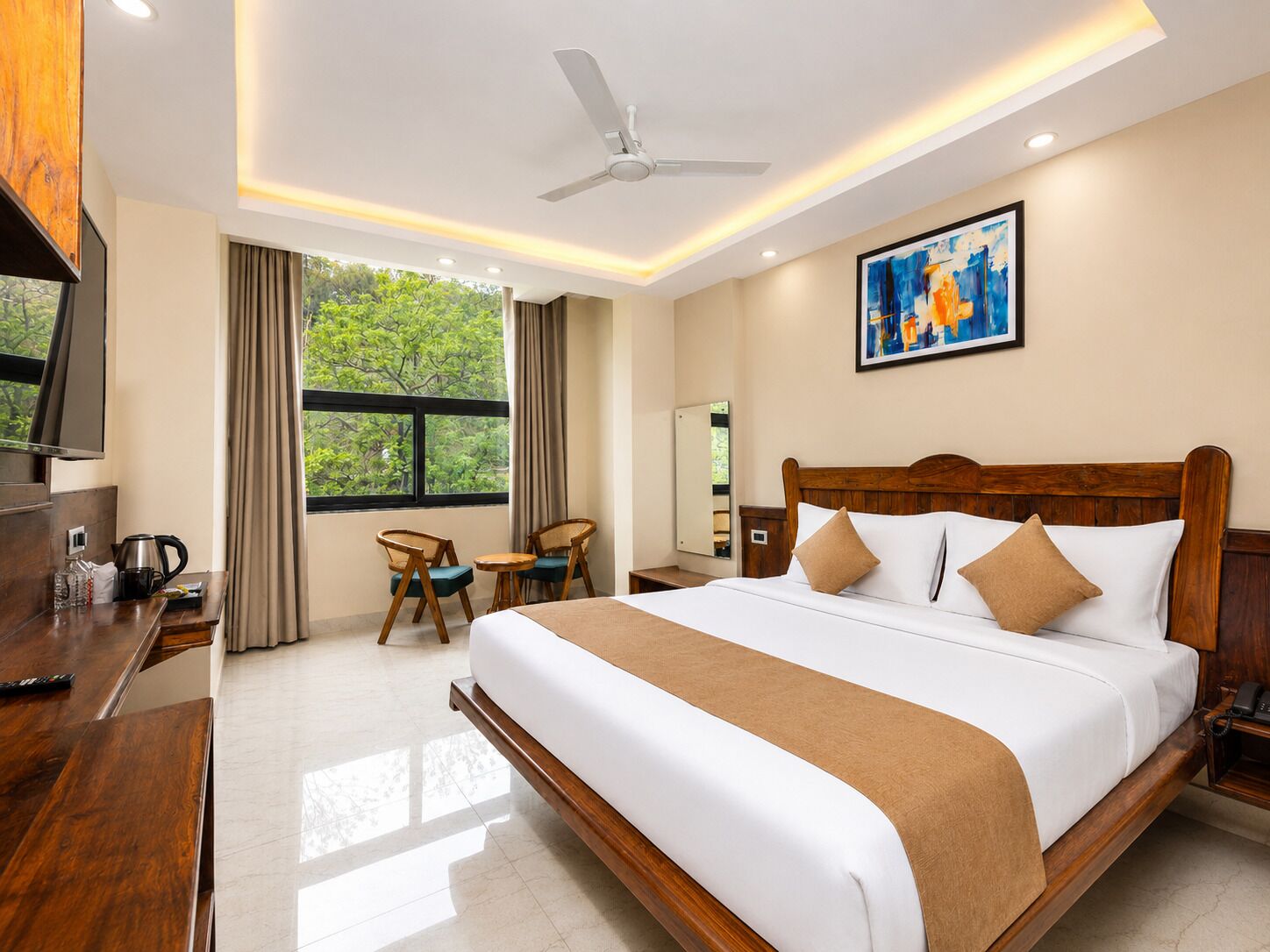 Habitación de hotel con una cama grande, un escritorio con televisor, una silla, una ventana con cortinas y un ventilador de techo.