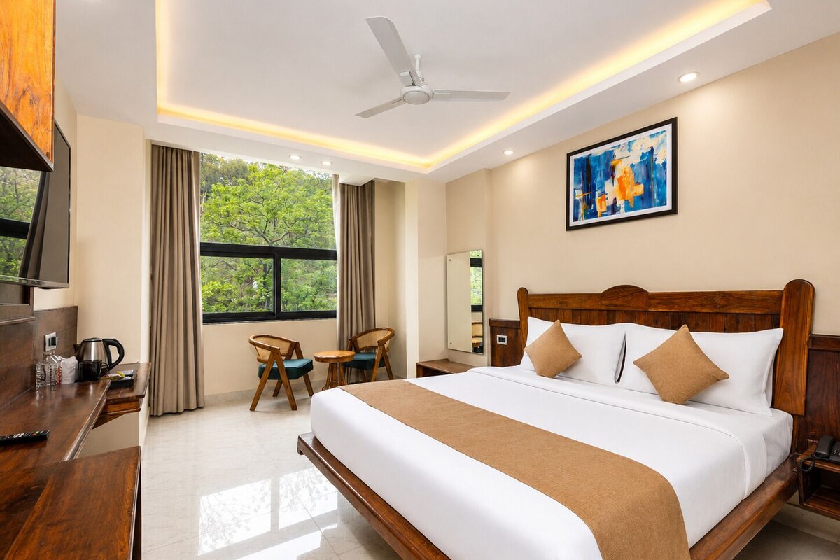 Habitación de hotel con una cama grande, un escritorio con televisor, una silla, una ventana con cortinas y un ventilador de techo.