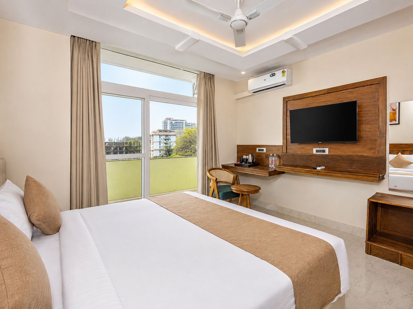 Una habitación de hotel con cama, escritorio, silla, televisor y aire acondicionado.