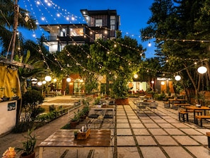 An outdoor patio area with tables and chairs, string lights, and potted plants.
