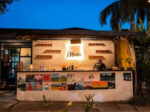 A bar with a neon sign, shelves with bottles, and a wall decorated with colorful paintings.