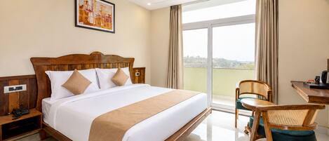 A hotel room with a large bed, a desk, a chair, a ceiling fan, and a window with curtains.