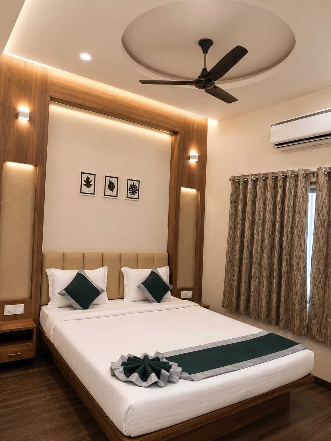 A hotel room with a bed, a ceiling fan, wall-mounted air conditioning, and framed leaf artwork.