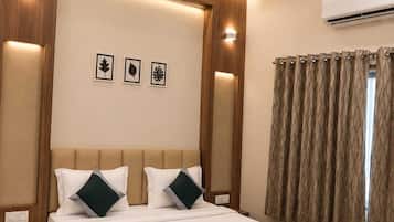 A hotel room with a bed, a ceiling fan, wall-mounted air conditioning, and framed leaf artwork.