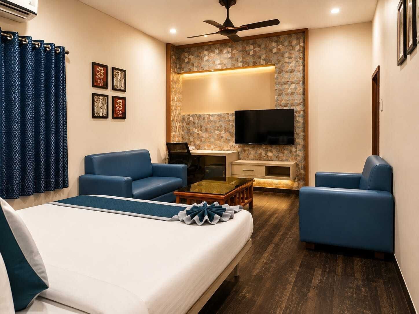 A hotel room with a bed, two blue sofas, a coffee table, a TV, and a desk.