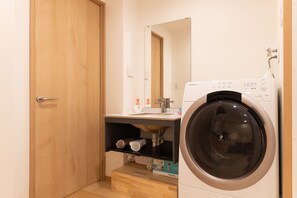 A compact bathroom with a washing machine, a sink, and a mirror.