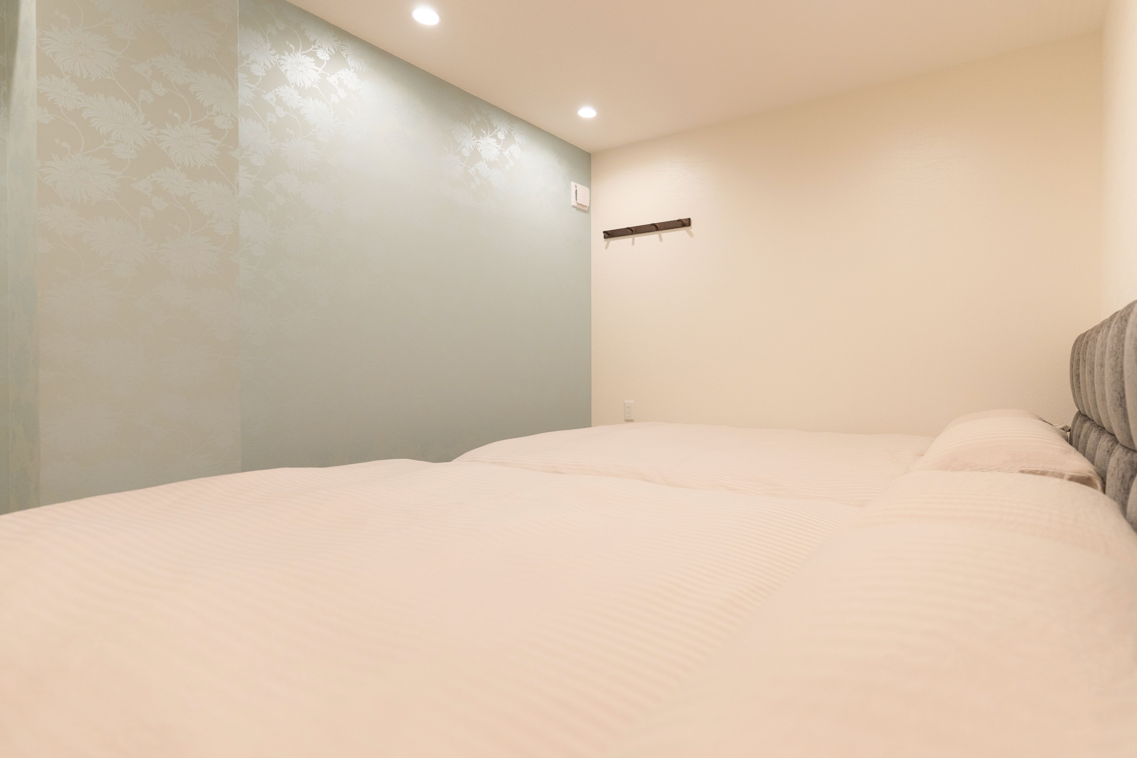 A bedroom with a bed, a wall-mounted shelf, and a ceiling light.