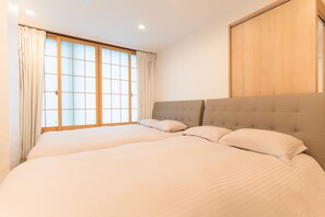 A bedroom with two beds, a large window with curtains, and a wooden wardrobe.