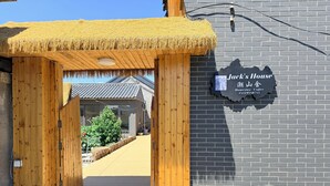 A wooden entrance with a thatched roof leading to a building with a brick facade and a sign reading 'Jack's House Homestay Coffee.'