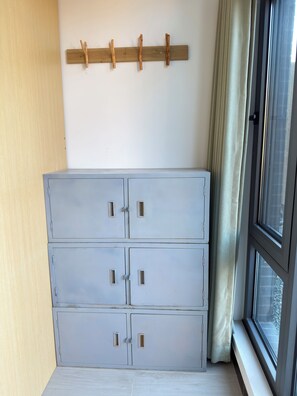 A room with a grey metal cabinet, a wooden coat rack, and a window with curtains.