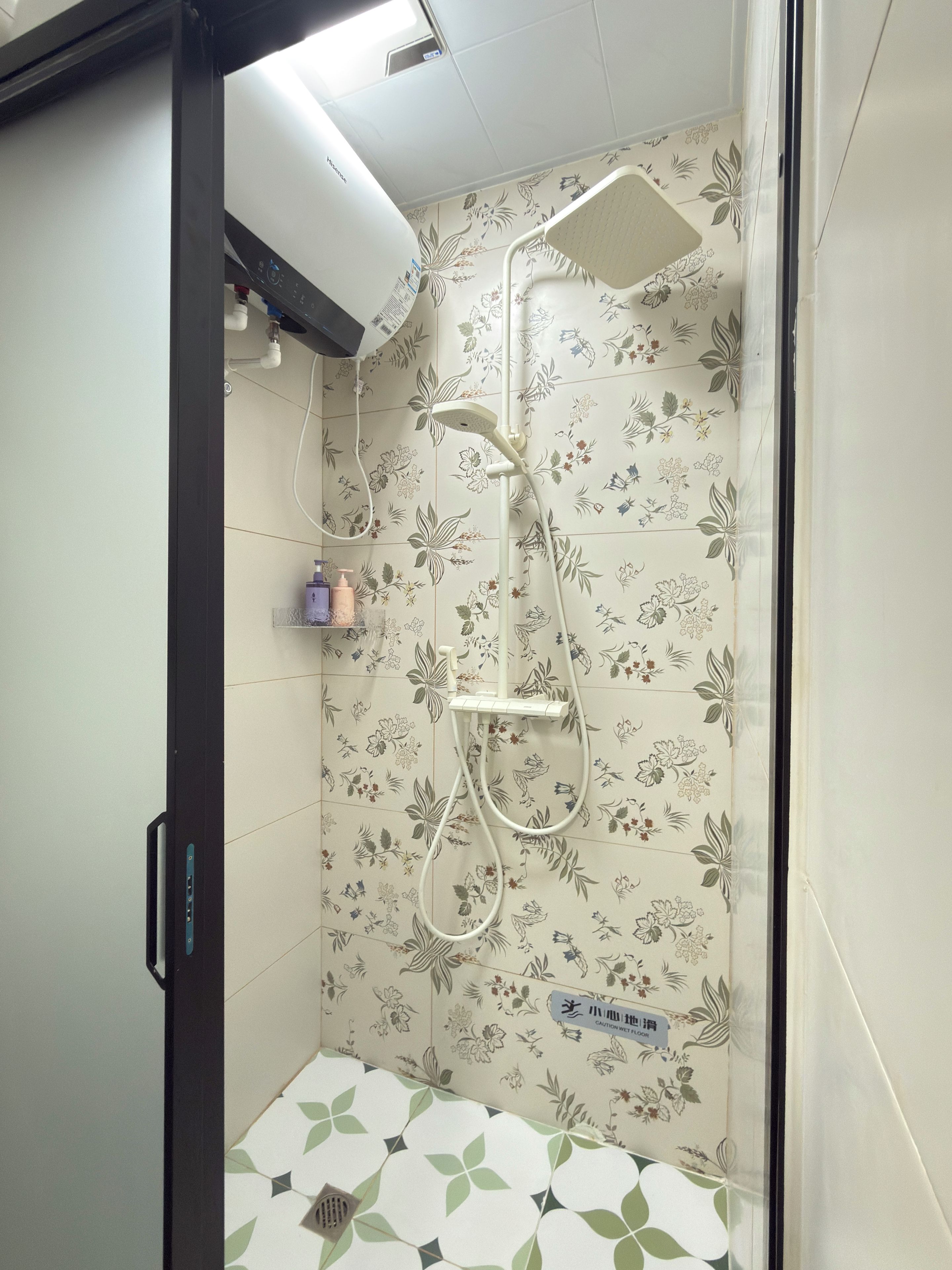 Una ducha con un estampado de baldosas florales, un cabezal de ducha manual y un panel de control en la pared.