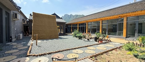 Un patio con un edificio tradicional, una estructura moderna con grandes ventanales y un banco de madera.