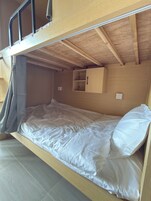 A bunk bed with a wooden headboard, a small cabinet, and a grey curtain.