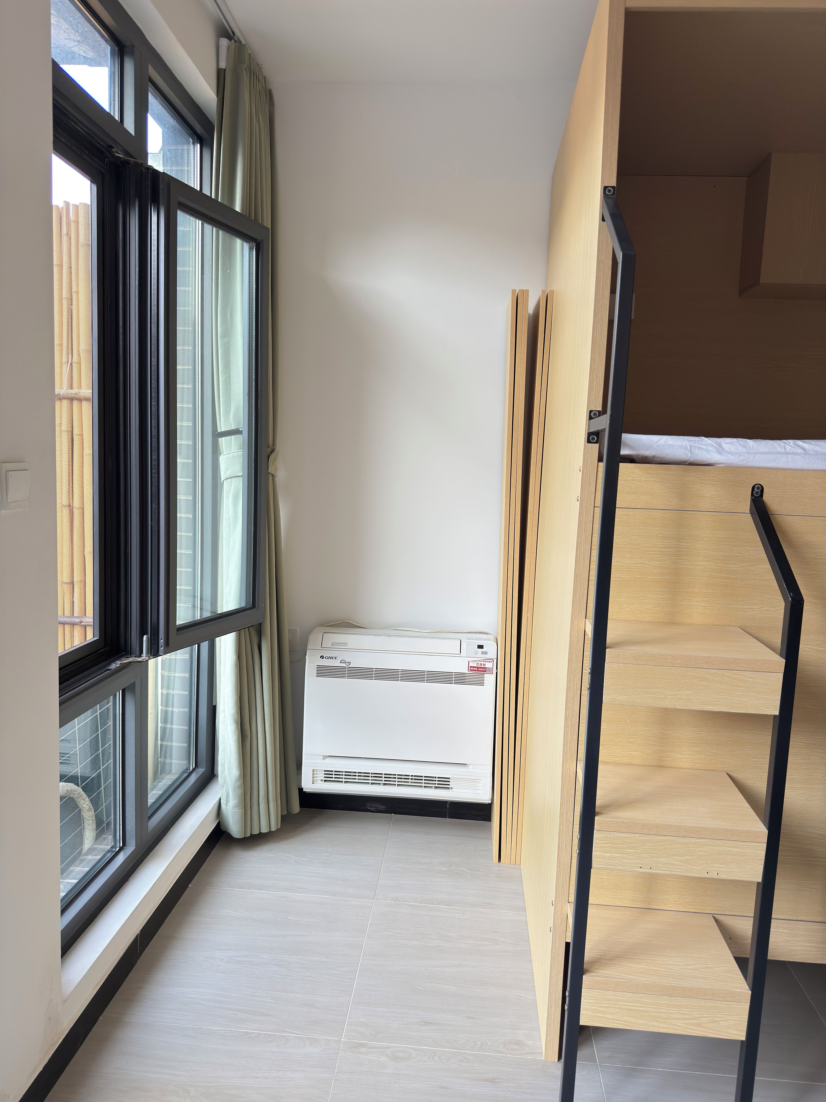 A room with a window, an air conditioning unit, and a wooden staircase.