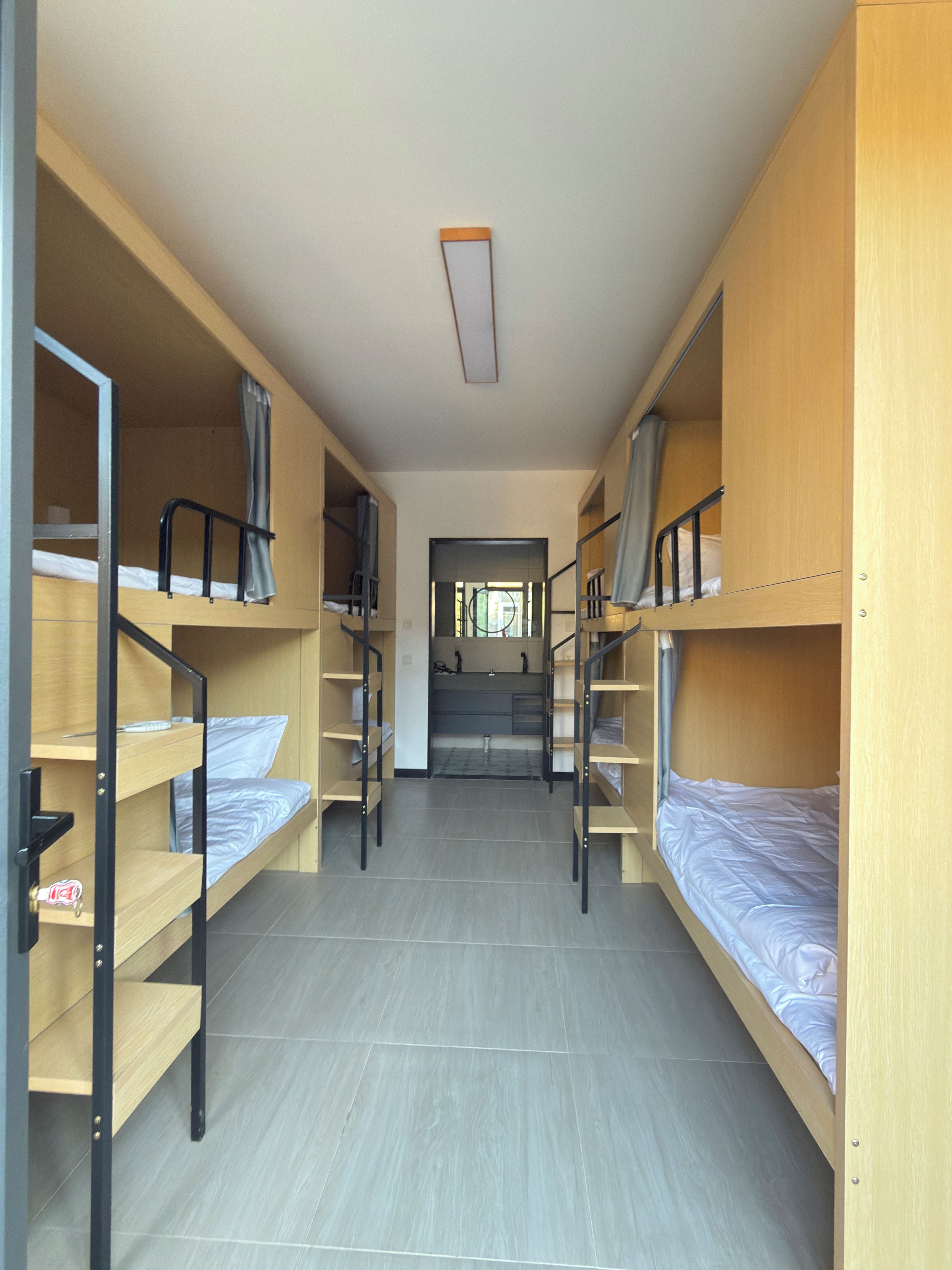 Un pasillo con literas a ambos lados, que conduce a un área de baño.