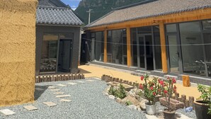 A traditional building with a tiled roof and large windows, surrounded by a gravel courtyard with potted plants and a wooden deck.