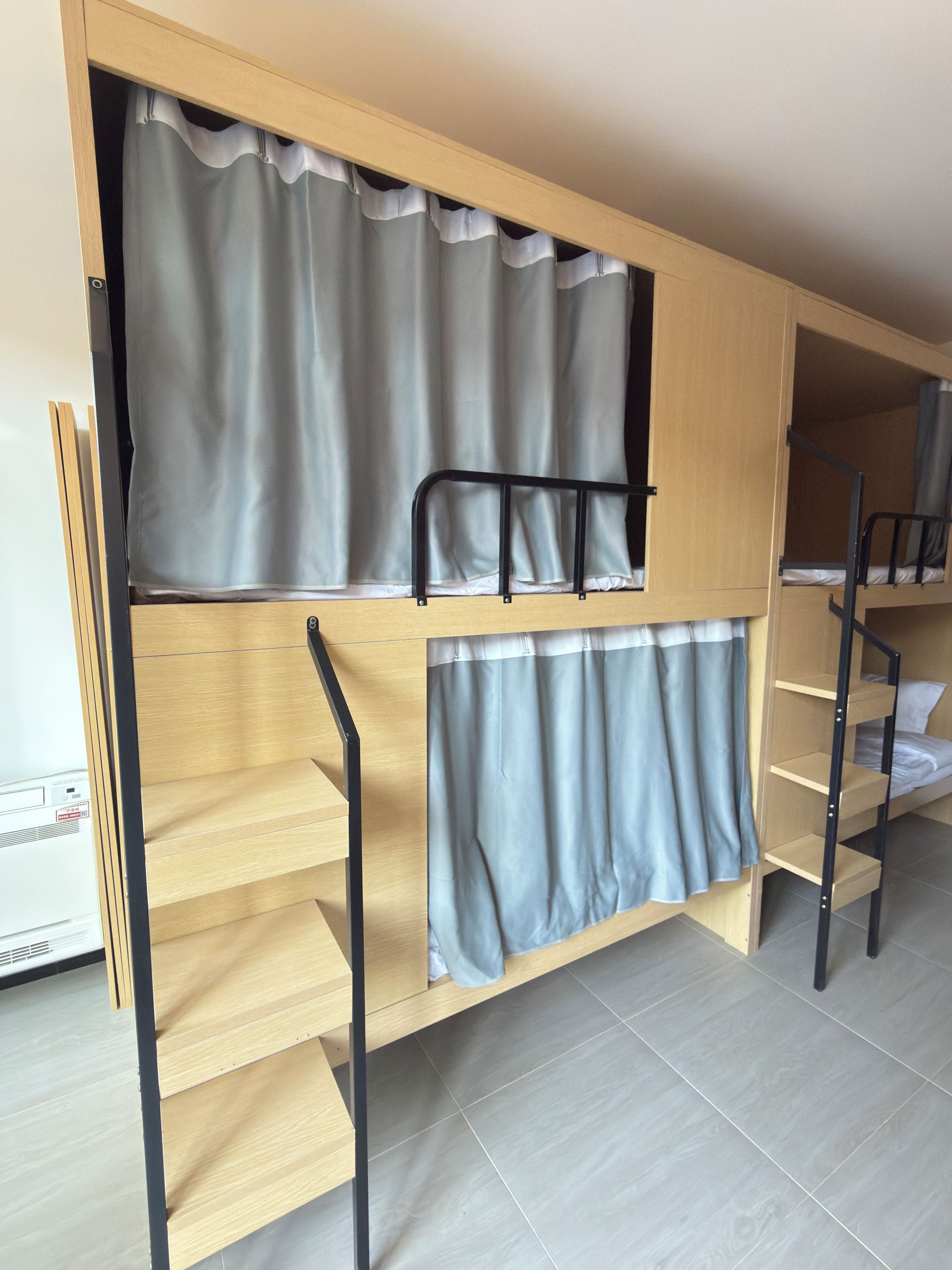Una cama litera con cortina, un estante pequeño y una escalera.
