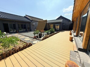 Une cour dotée d’une terrasse en bois, de plantes en pot et de bâtiments traditionnels aux toits de tuiles.