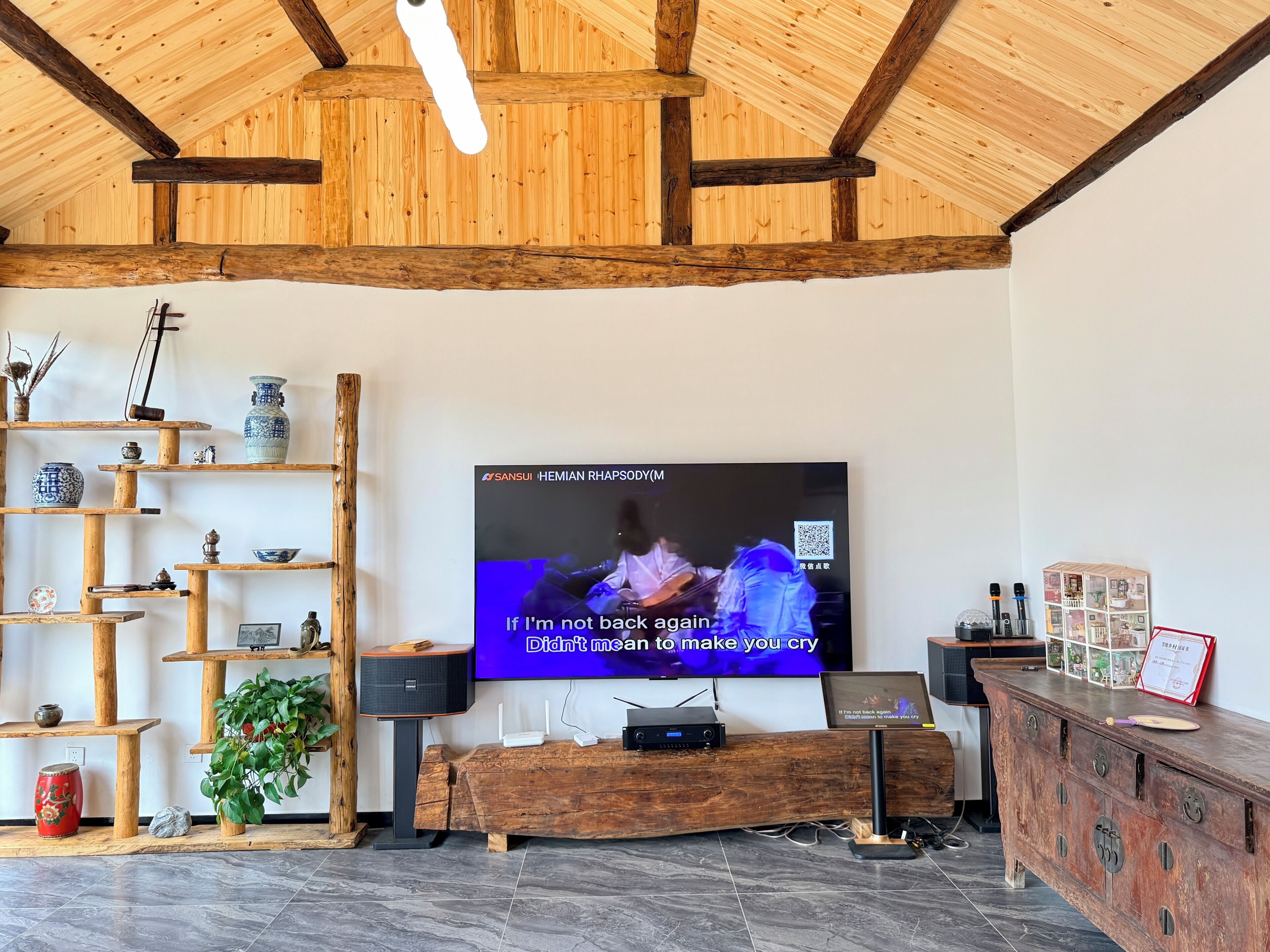 A room with a wooden ceiling, a television mounted on the wall, and a wooden cabinet with drawers.