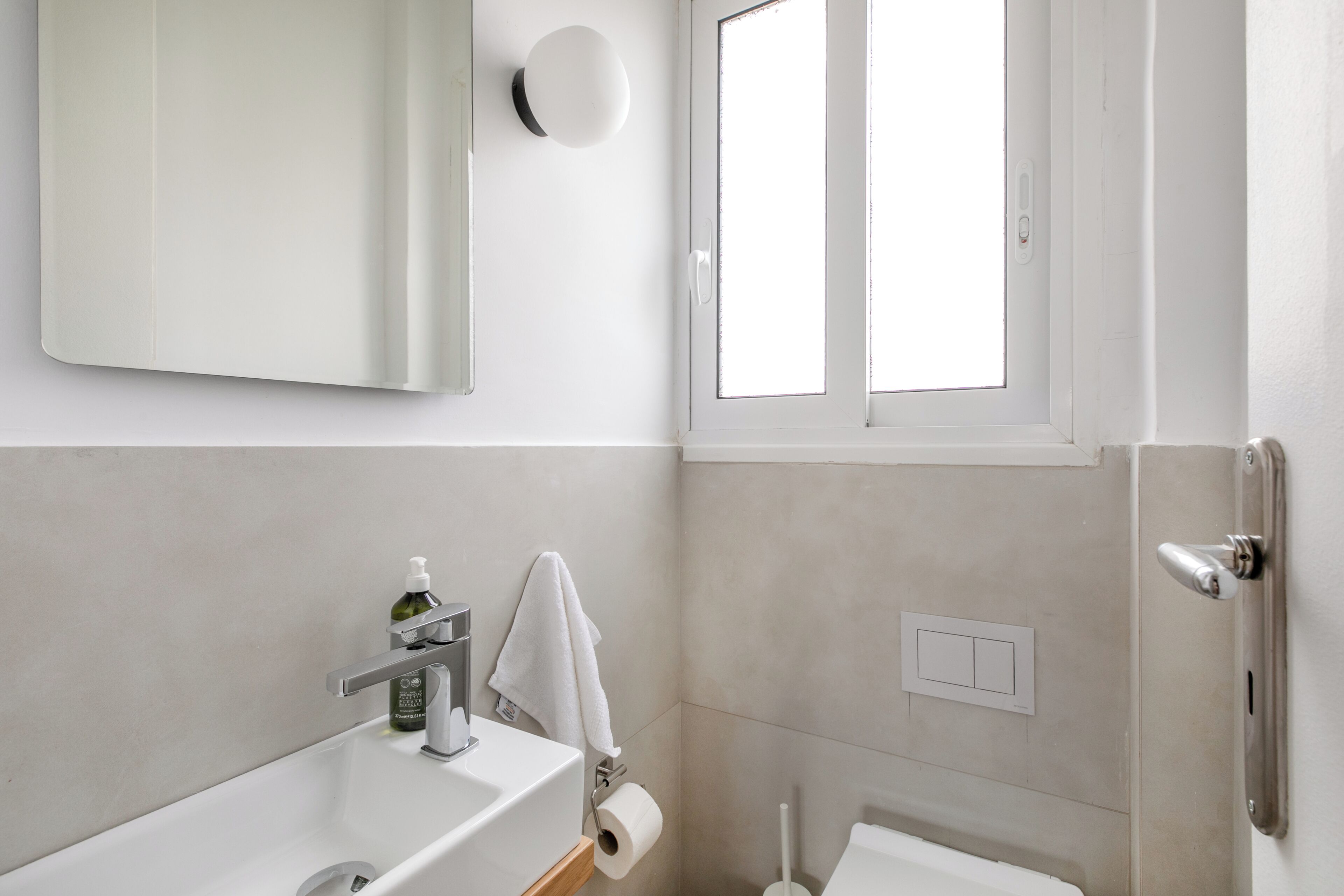 Un baño con lavamanos blanco, espejo, toalla, inodoro y ventana.