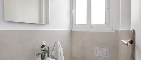 Un baño con lavamanos blanco, espejo, toalla, inodoro y ventana.