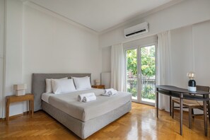 A hotel room with a bed, a table, and a chair. There is an air conditioning unit on the wall. - Thriasion 10 Atelier (Athens)