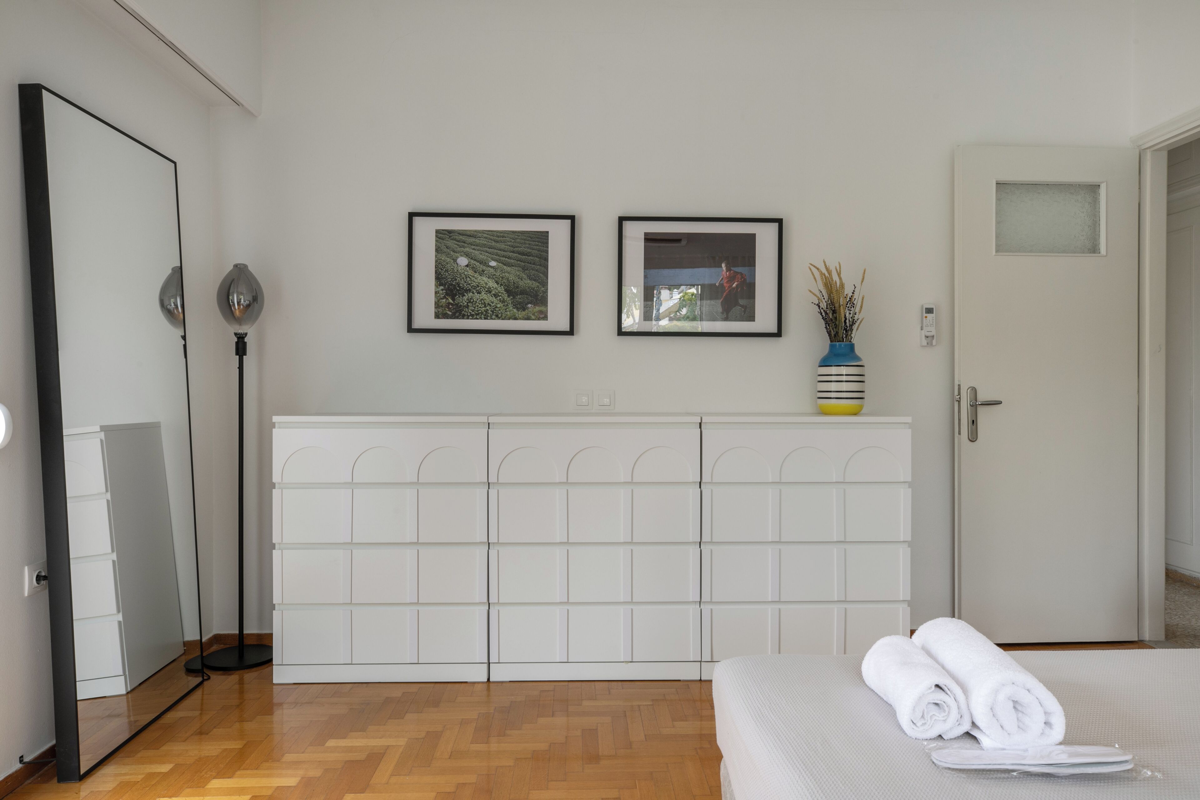A hotel room with a bed, a wardrobe, a mirror, and two framed pictures on the wall.