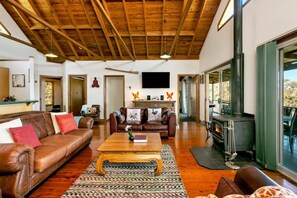 Ein geräumiges Wohnzimmer mit Holzbalkendecke, Kamin, Fernseher und großem Fenster.