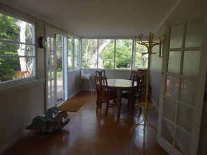Ein Wintergarten mit Esstisch, Stühlen, einer Uhr und einem Garderobenständer.