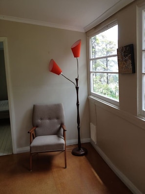 Ein Eckzimmer mit Stuhl, Stehlampe und Fenster mit Blick auf Bäume.