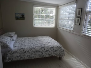 Ein Schlafzimmer mit einem Bett, zwei Fenstern mit Jalousien, einem kleinen Gemälde an der Wand und einer Heizung.