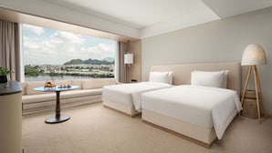 Ein Hotelzimmer mit zwei Betten, einem Sofa, einem runden Tisch mit Obstschale und Blick auf Stadt und Berge.