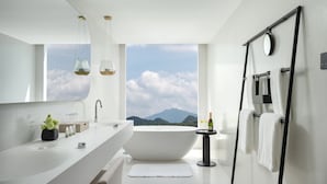 Ein modernes Badezimmer mit einer großzügigen Badewanne, einem Doppelwaschtisch und einem großen Fenster mit Blick auf die Berge.