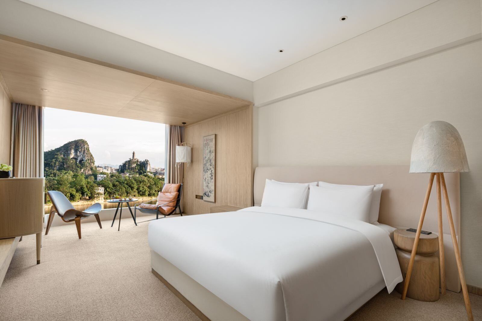 Habitació d'hotel amb un llit gran, escriptori, dues cadires, una làmpada i vista a un paisatge de muntanya.