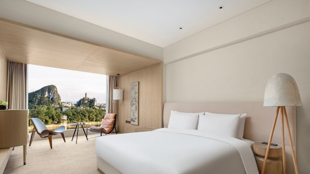 Ein Hotelzimmer mit einem großen Bett, einem Schreibtisch, zwei Stühlen, einer Lampe und Blick auf eine Berglandschaft.