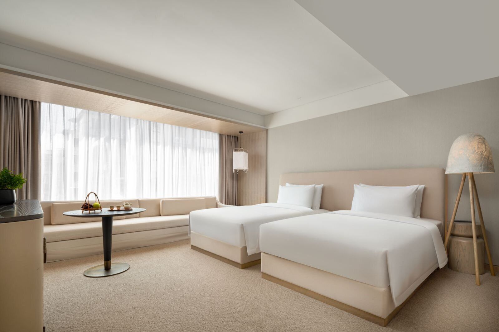 A hotel room with two beds, a sofa, a small table with a plant, and a lamp.
