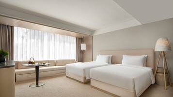 A hotel room with two beds, a sofa, a small table with a plant, and a lamp.