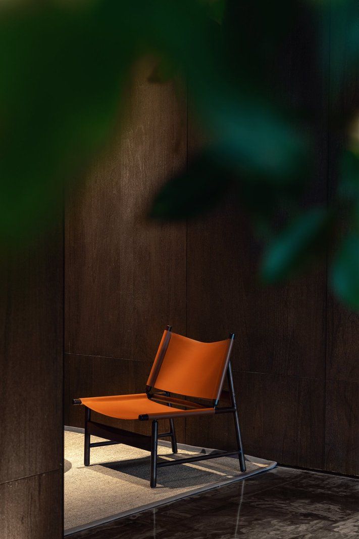 Une seule chaise orange à armature métallique, placée contre un mur en bois foncé.