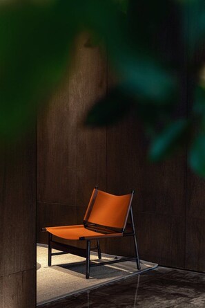 A single orange chair with a metal frame, positioned against a dark wooden wall.