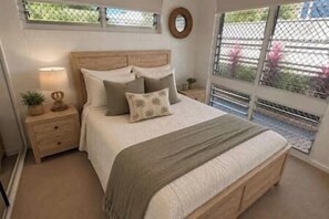 Ein Schlafzimmer mit einem Holzbett, einem Nachttisch, einer Lampe und Blick durch ein Fenster.