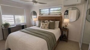 Um quarto com cama, mesas de cabeceira, espelho e janela.