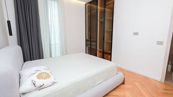 Un dormitorio moderno con cama, un ventanal con cortinas, un armario con puertas de cristal y suelo de madera.