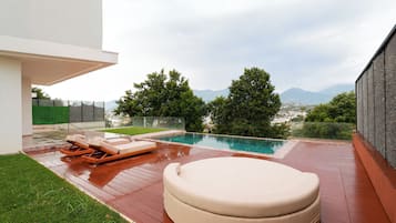 A modern outdoor pool area with a wooden deck, lounge chairs, and a seating area.