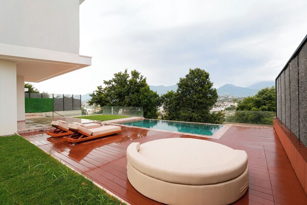 A modern outdoor pool area with a wooden deck, lounge chairs, and a seating area.