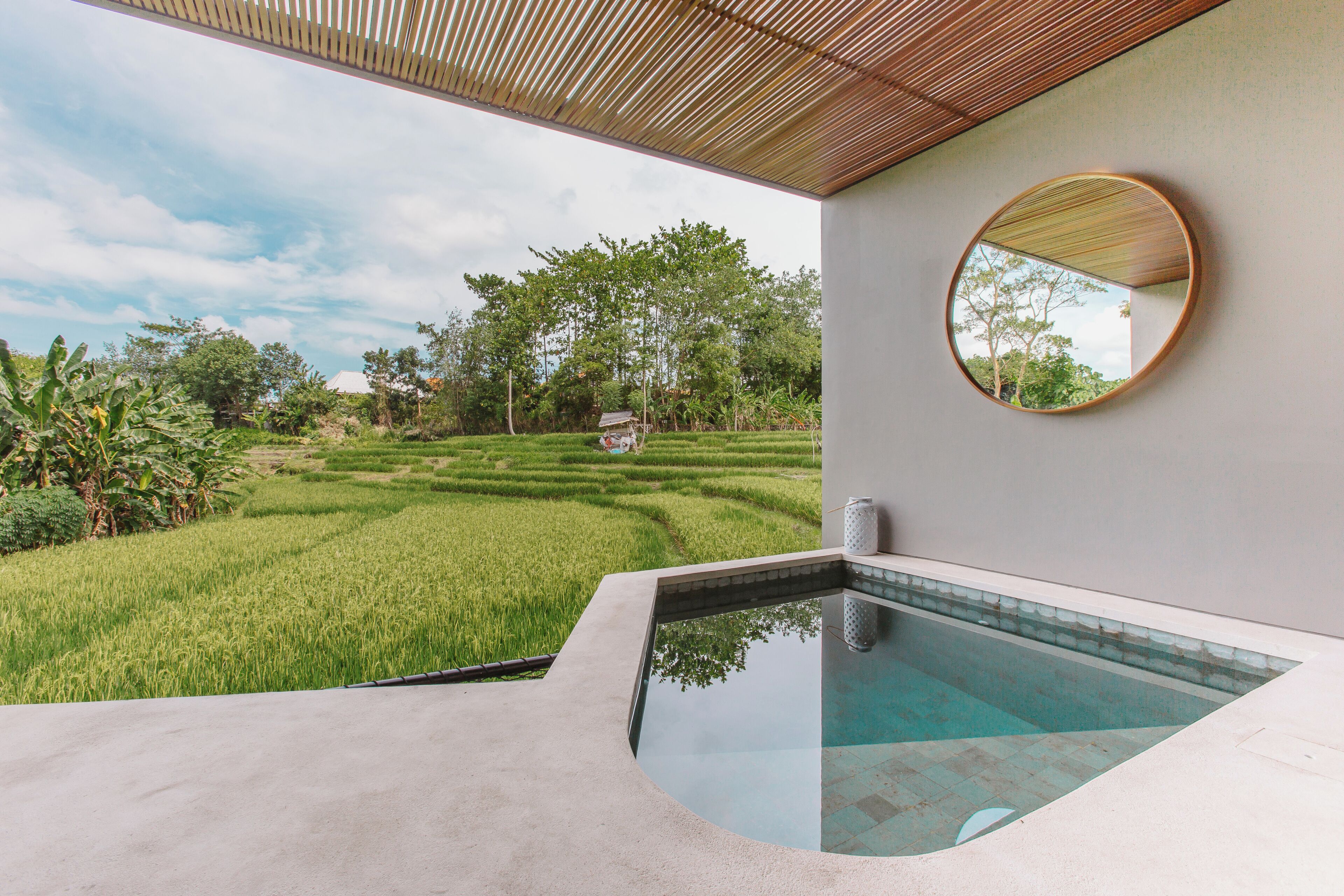 A modern pool area with a view of a lush green landscape and a traditional hut in the distance.