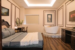 Ein Schlafzimmer mit Bett, Schreibtisch, Stuhl, Fenster, Badewanne und Fernseher.