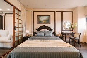 Ein Schlafzimmer mit einem Bett, einem Schreibtisch, einem Sessel, einem Nachttisch, einem Spiegel und einem Bild an der Wand.